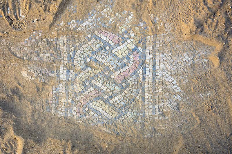 Dirt and sand has been brushed away to reveal Mosaic tiles beneath it.