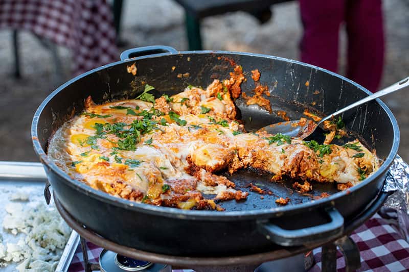 A half eaten skillet of cooked breakfast made with eggs, tomatoes, onion, peppers, and spices.