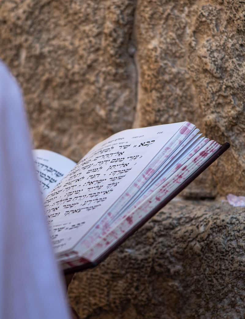 A man holds a Hebrew bible next to a wall.