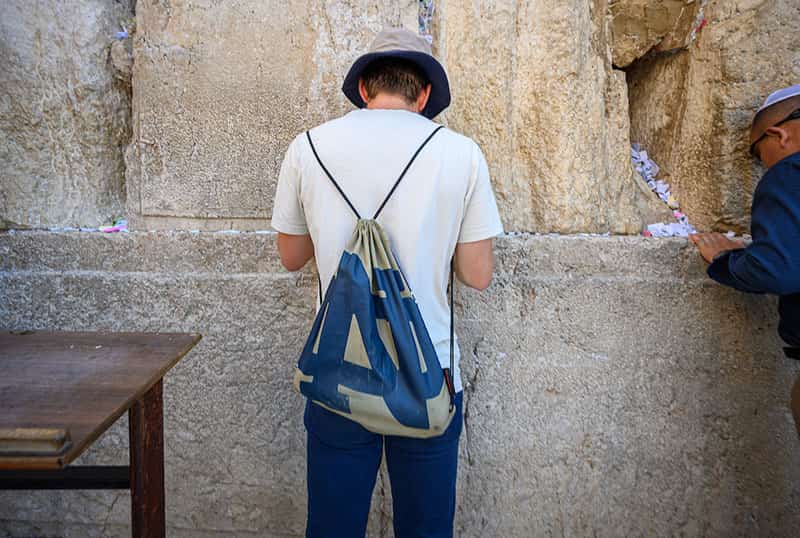 A student stands and faces with their head down at the Wester Wall.
