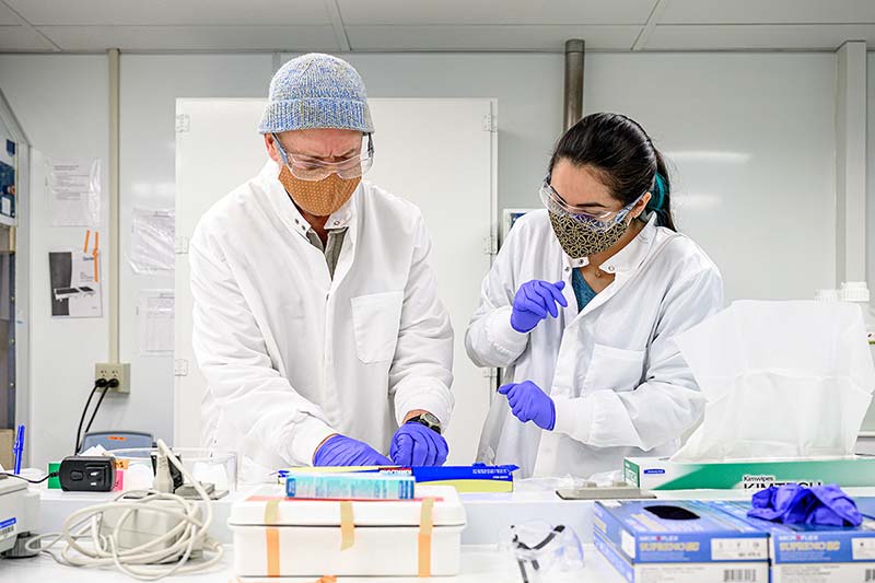 Two people	wearing lab coats, masks, rubber gloves, and eye protection process samples of lunar rock and dust.
