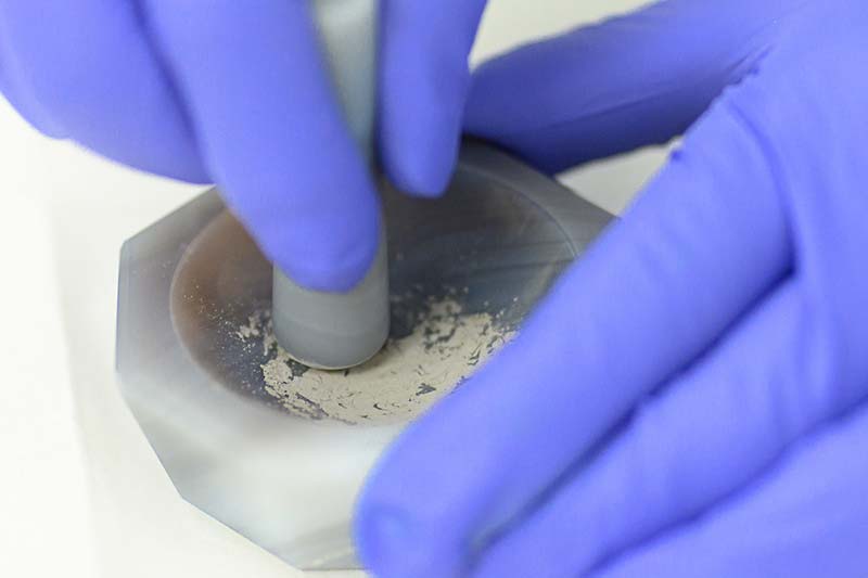 A close up shot of hands wearing rubber gloves grinding samples of lunar rock.