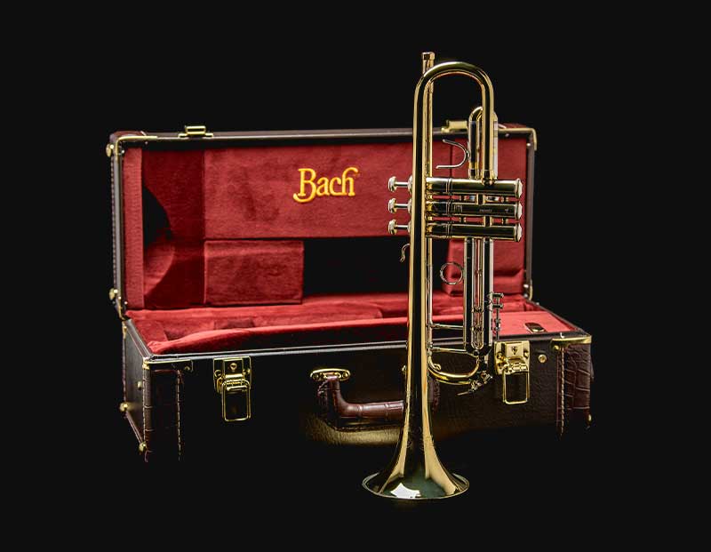 Trumpet standing on its bell, an open case lined in red cloth is open behind it with the text Bach in gold