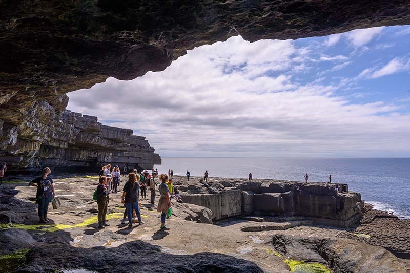People stand on a stony cliff with overhanging cave.