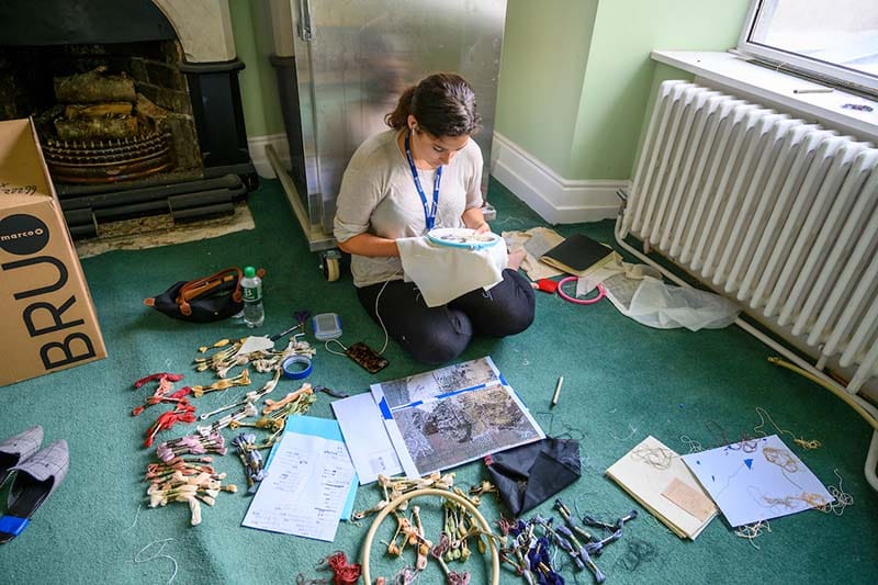 A girl sits on the floor surrounded by embroidery thread.