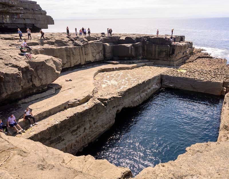 A natural perfectly rectangular pool on the island. People stand around it.
