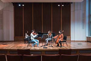 A group of four student musicians perform together on a stage.