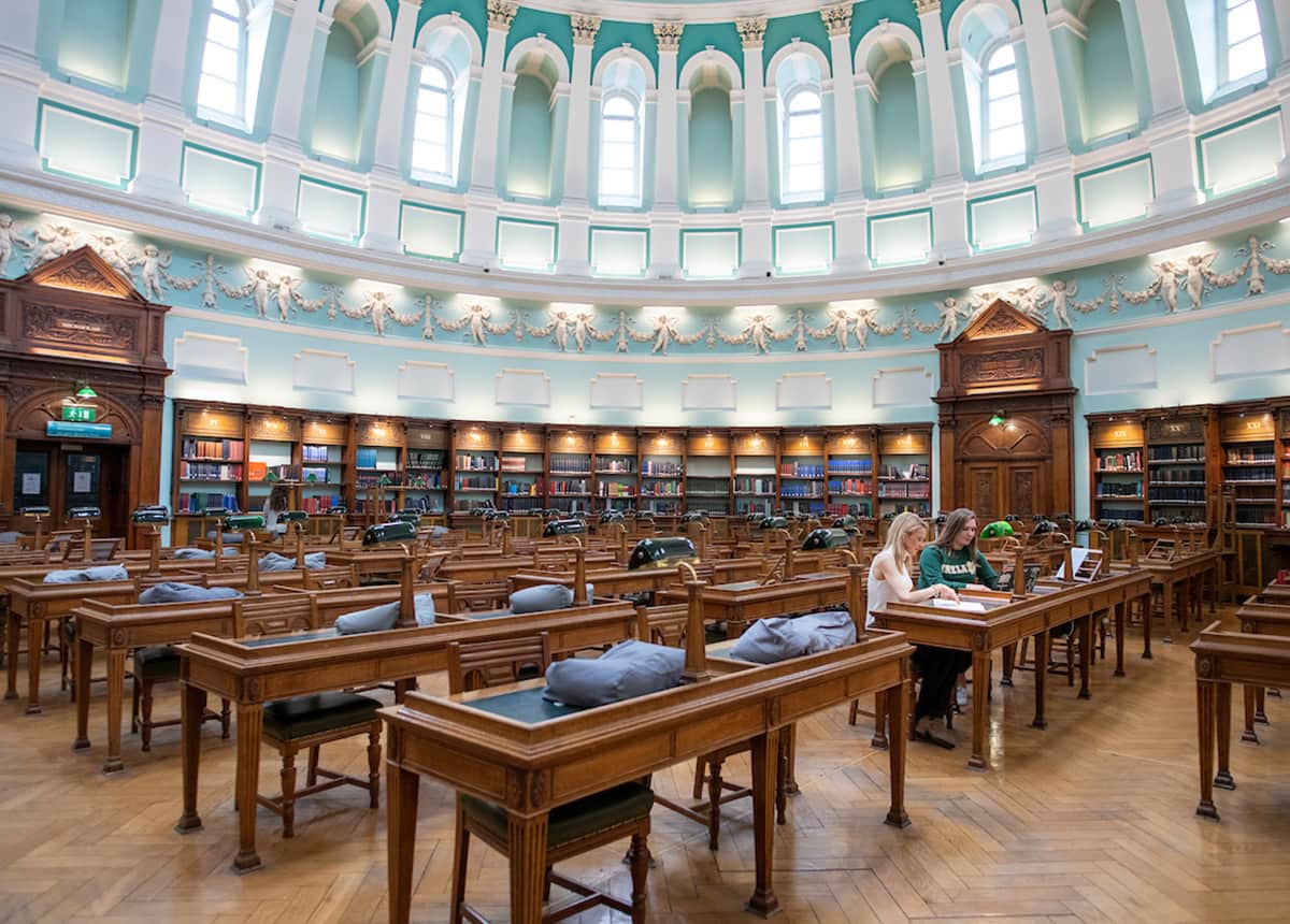 Two female students sit at one of the many desks inside a library.