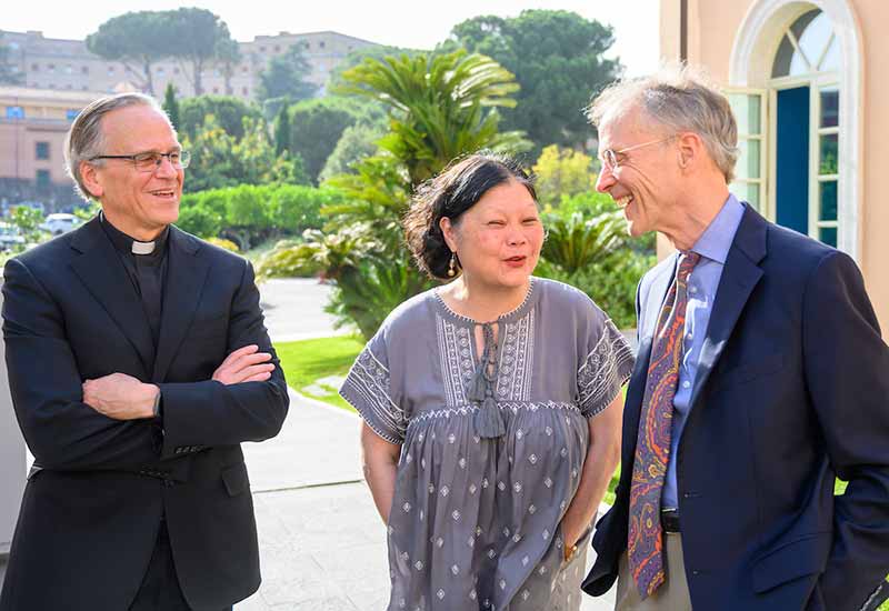 Three people stand outside near the Vatican in Rome and have a discussion.
