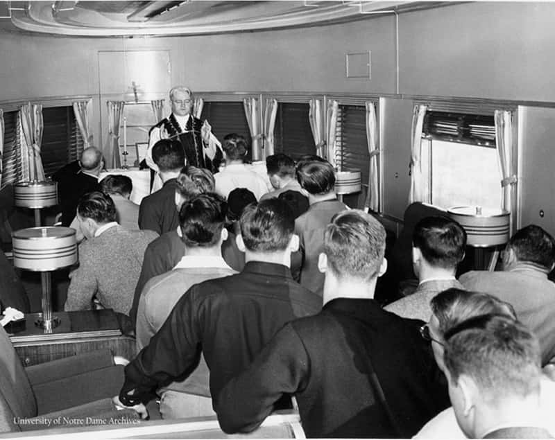 A black and white photo of a football team have mass inside a small trailer.