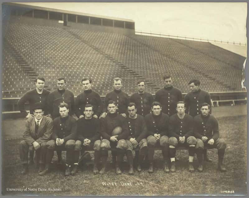 A black and white photo of football team pose for a team photo on a football field.