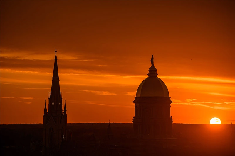A sunset behind the silhouettes of the Golden Dome and Basilica of the sacred heart