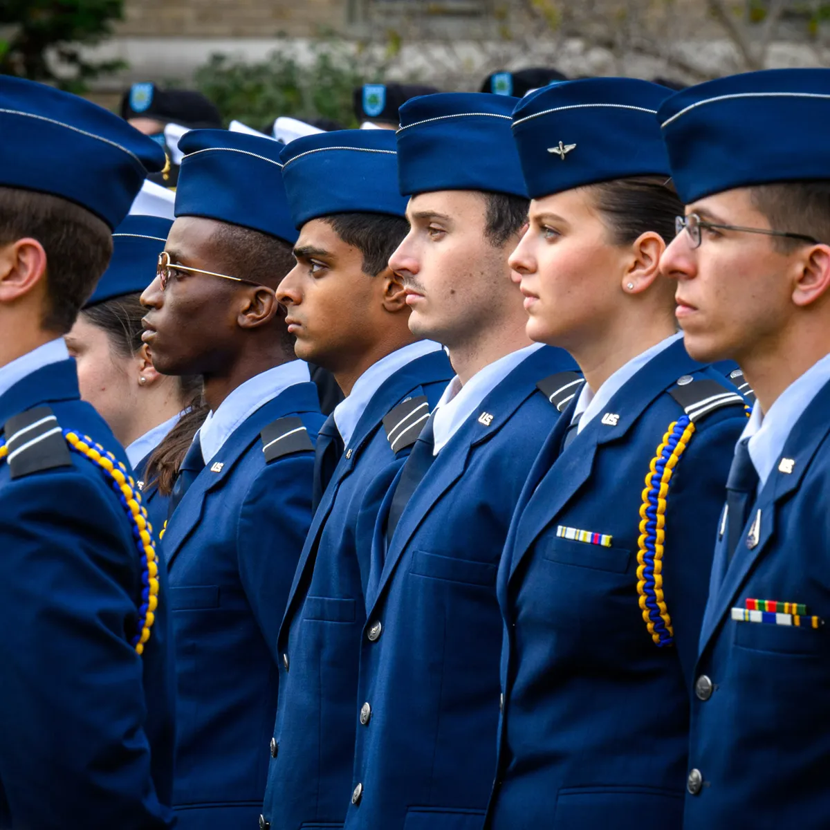A group of Air Force ROTC cadets in blue uniforms stand in formation, with a diverse line of five cadets visible in profile.