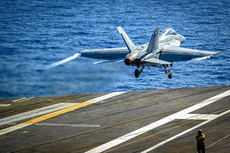 A gray fighter jet with the number '240' on its wings performs a catapult launch from the deck of an aircraft carrier over deep blue water.