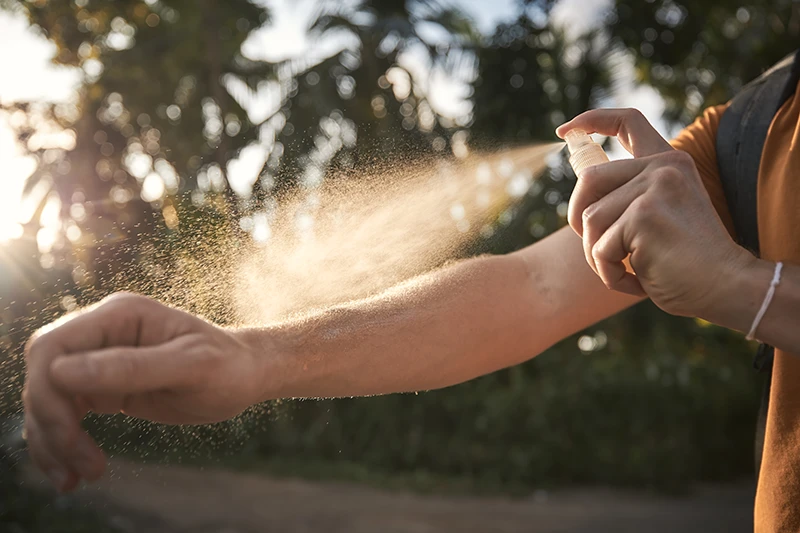A person spraying insect repellent on their arm.