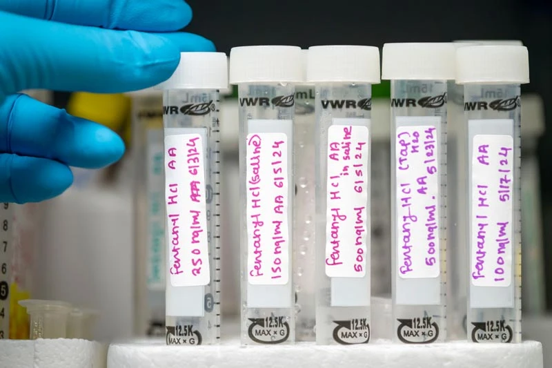 A gloved hand places a test tube labeled 'Fentanyl HCl' into a rack with four other similar vials.