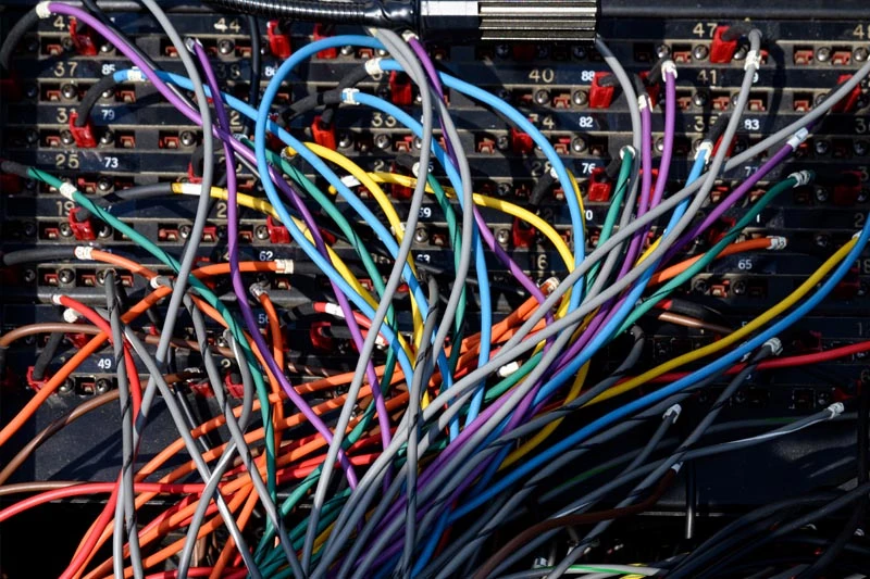 A close-up view of a tangled array of colorful wires plugged into a black patch panel.