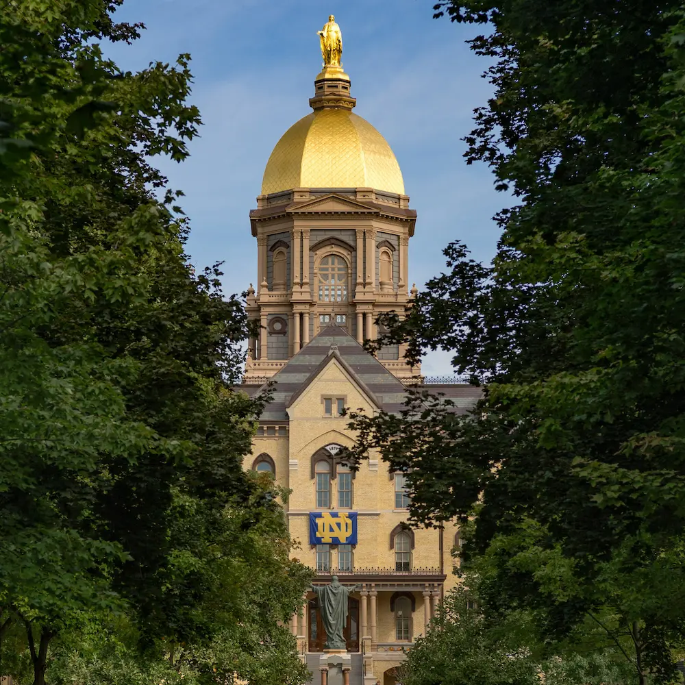 The Golden Dome and Main Building are framed by green trees on a bright day.