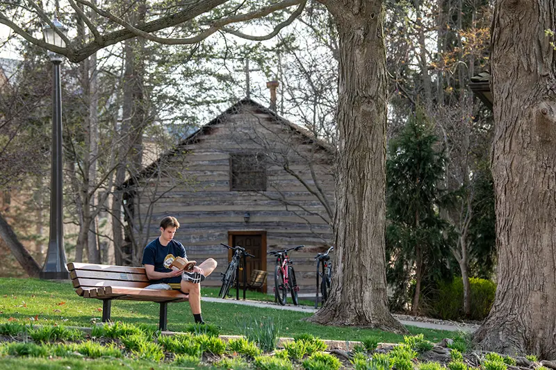 A student reads in front of the Log Chapel while enjoying the warmer weather and sunshine.